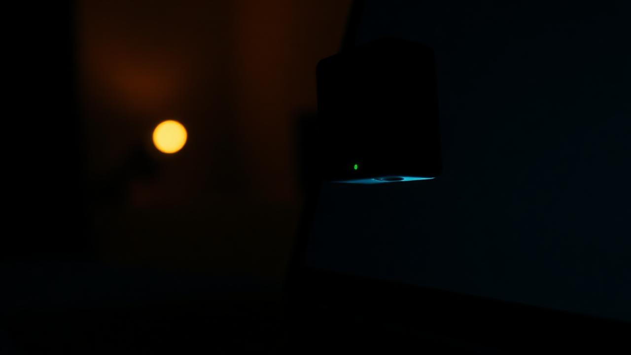 Close-up of a laptop webcam with green privacy LED on in a dark room, browser camera privacy concept