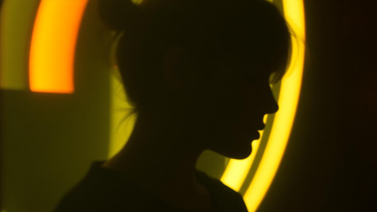 Motion-blurred portrait silhouette against warm tungsten ring light, suggesting an animated photobooth GIF loop